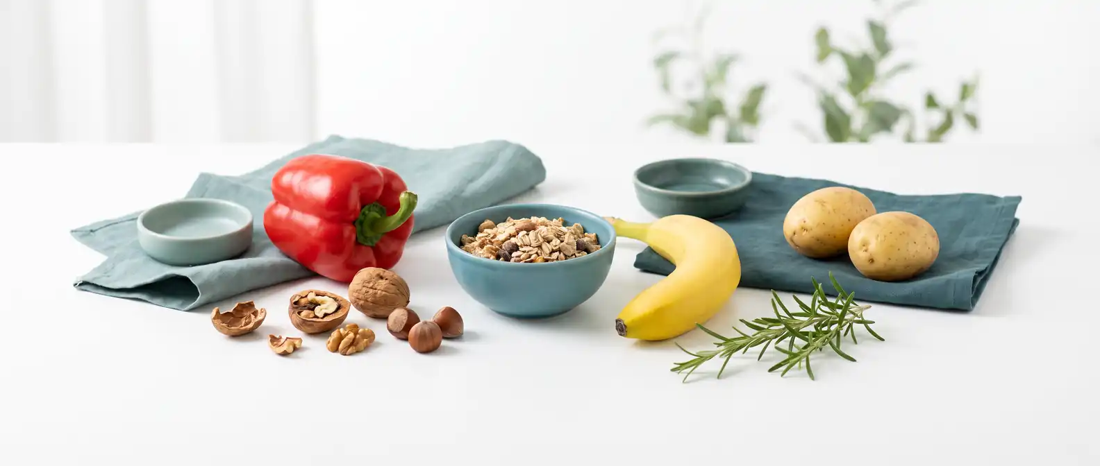Vitamin-B6-reiche Lebensmittel wie rote Paprika, Walnüsse, Vollkorn, Banane und Kartoffeln auf hellem Untergrund